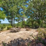 Stone patio with fire pit and outdoor kitchen under oaks on a Lindale property
