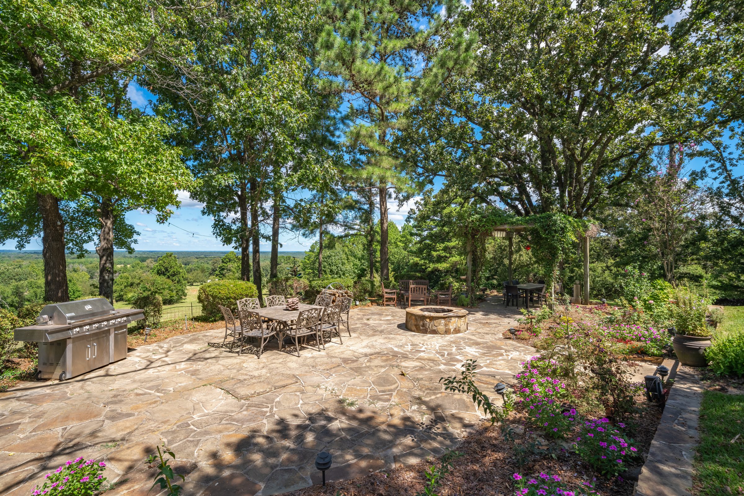 Stone patio with fire pit and outdoor kitchen under oaks on a Lindale property